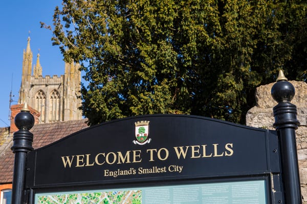 Wells, UK - March 16th 2020: A Welcome to Wells information board in the city of Wells, Somerset, UK.  The tower of St. Cuthbert Church is in the background.