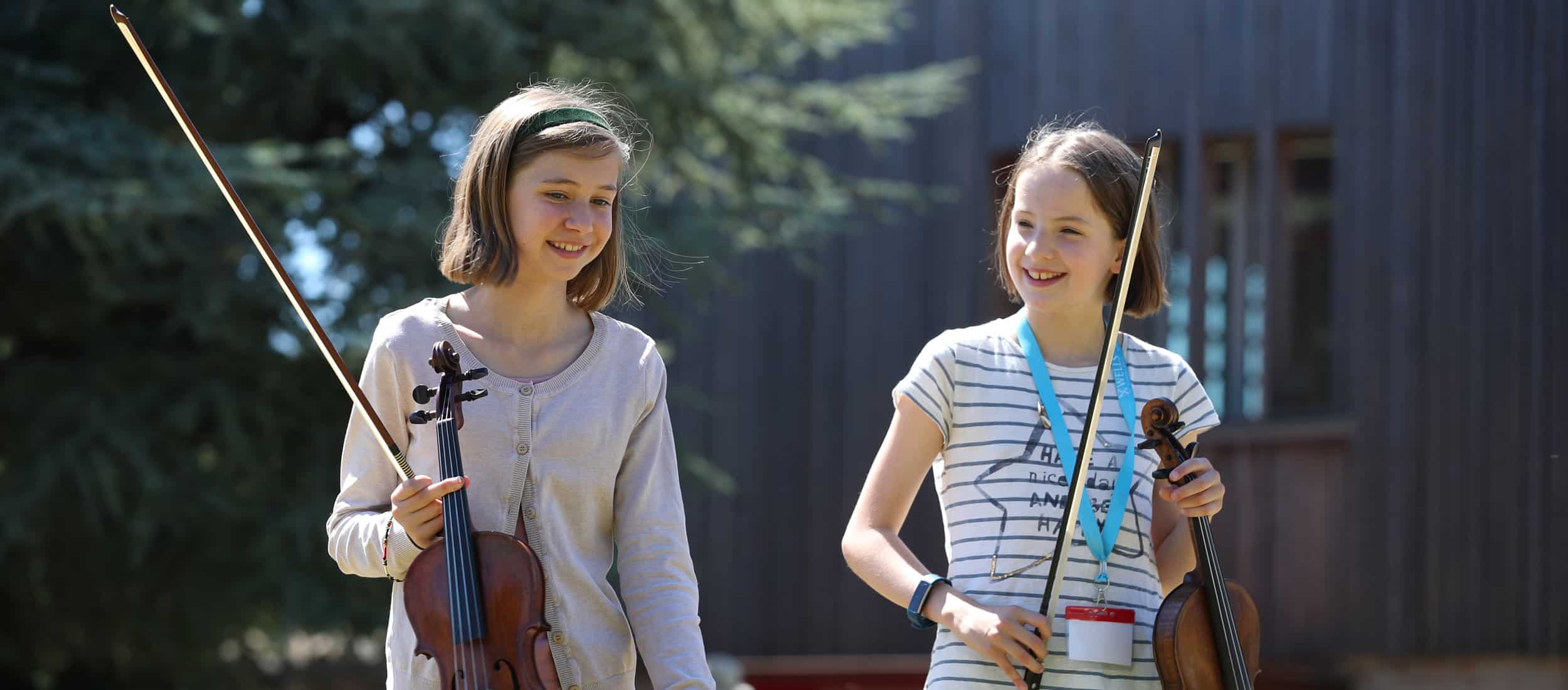 Two girls walking with violins at our Specialist Music School in England